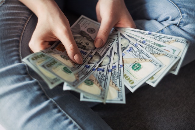 person in blue jeans holding several one hundred dollar bills